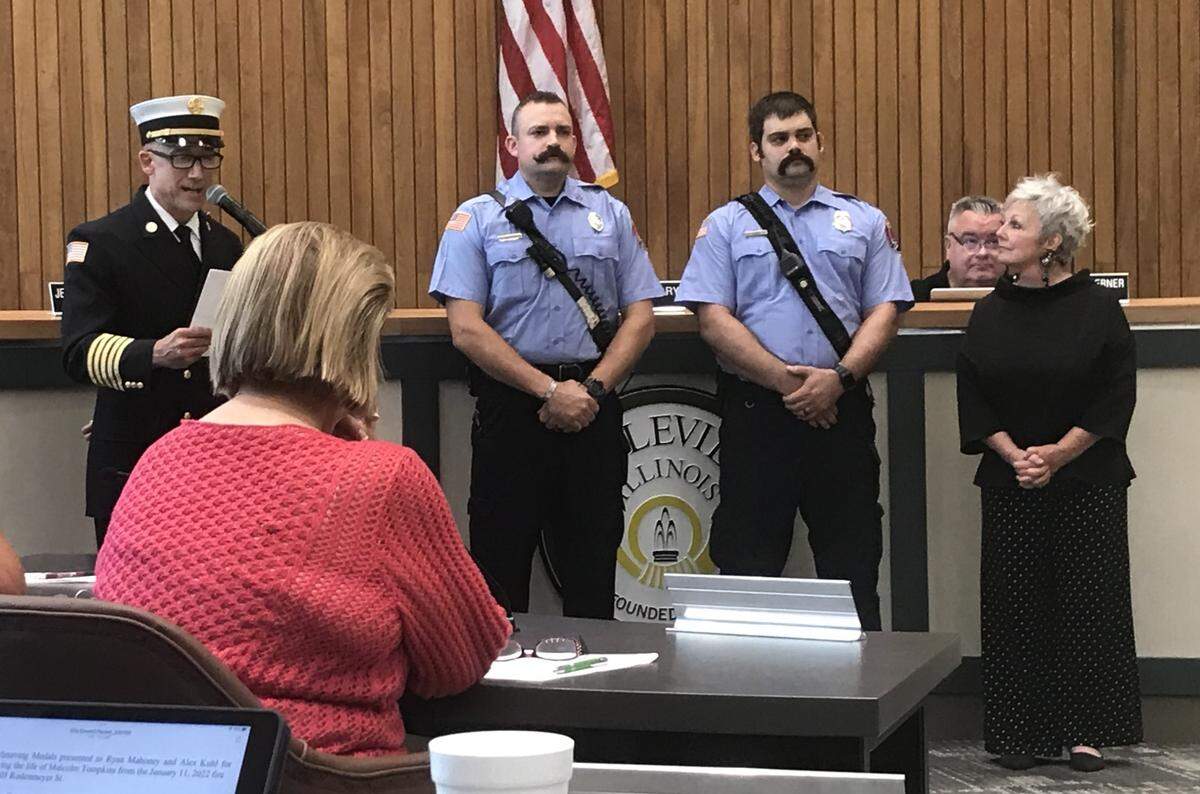 Belleville Fire Chief J.P. Penet, left to right, explains why firefighters Ryan Mahoney and Alex Kuhl are receiving Lifesaving Medals as Mayor Patty Gregory looks on at a Belleville City Council meeting Tuesday night.
