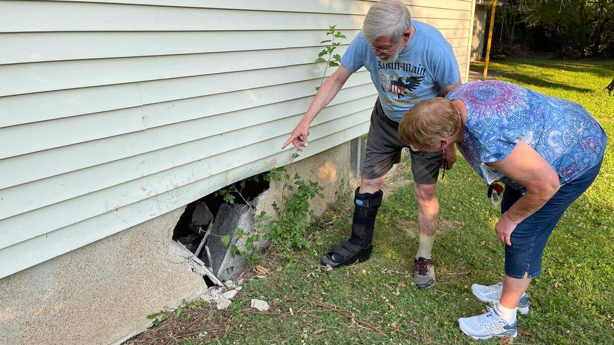 Fred Norton, left, shows his neighbor, Mary Eros, a hole caused June 28 by a car that missed a curve, jumped a curb, plowed through his yard and ran into his home on South 17th Street.
