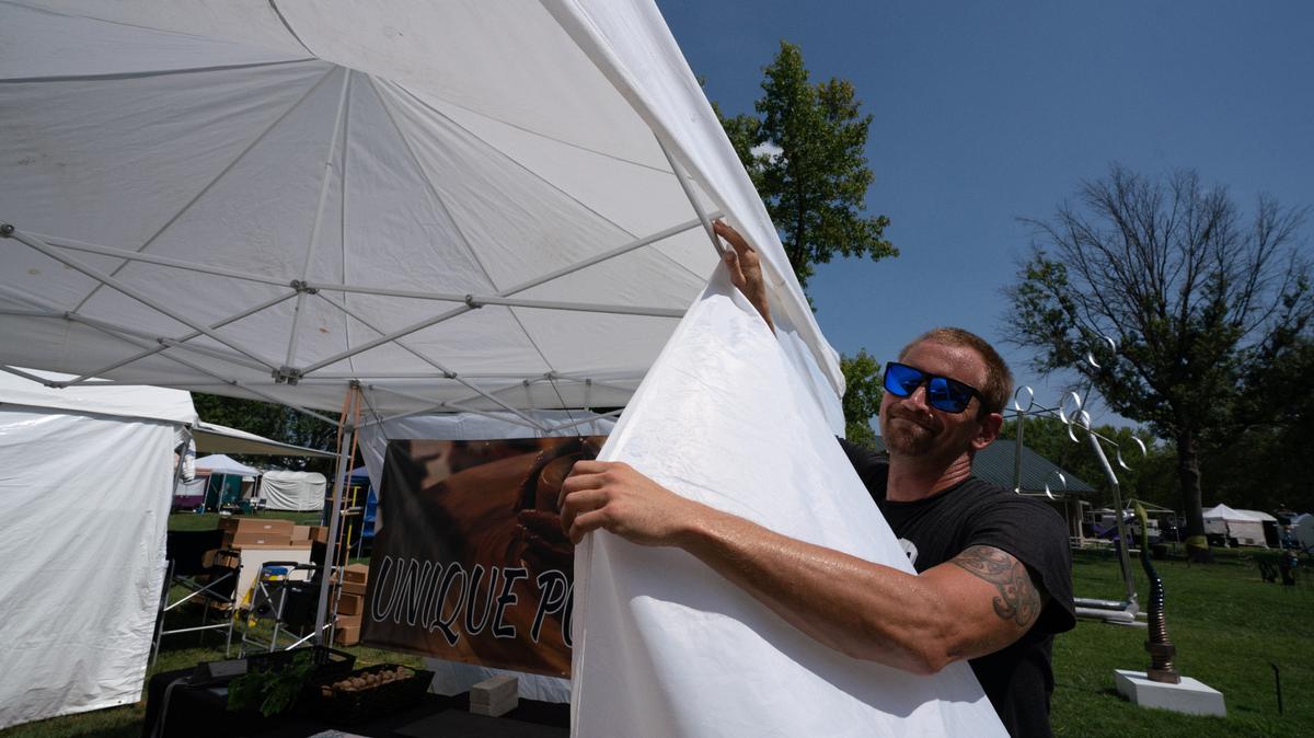 Phil Bonushkin, a ceramics artist, swelters in the heat as he hangs a tent in preparation for Fairview Heights’ Salute to the Arts festival on Aug. 25, 2023.