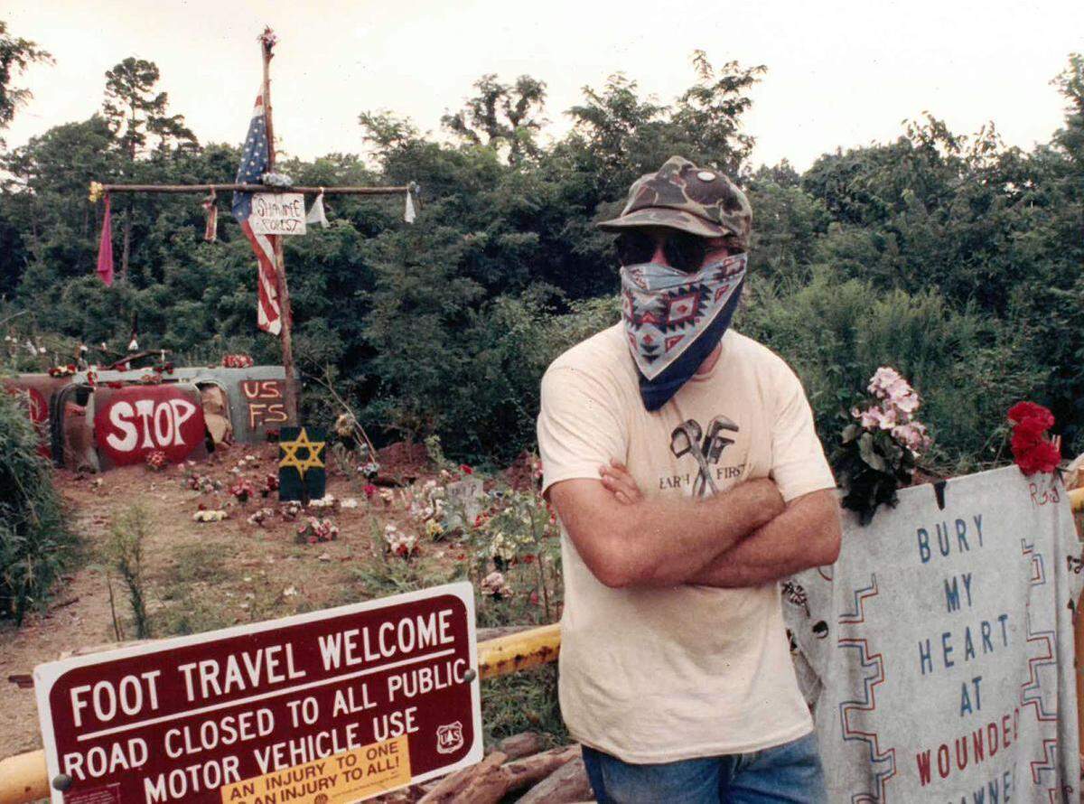 An anti-logging activist is seen outside of the Fairview camp Aug. 22, 1990. In the background is the buried Chevy Corvair activists affectionately referred to as “the biscuit.”