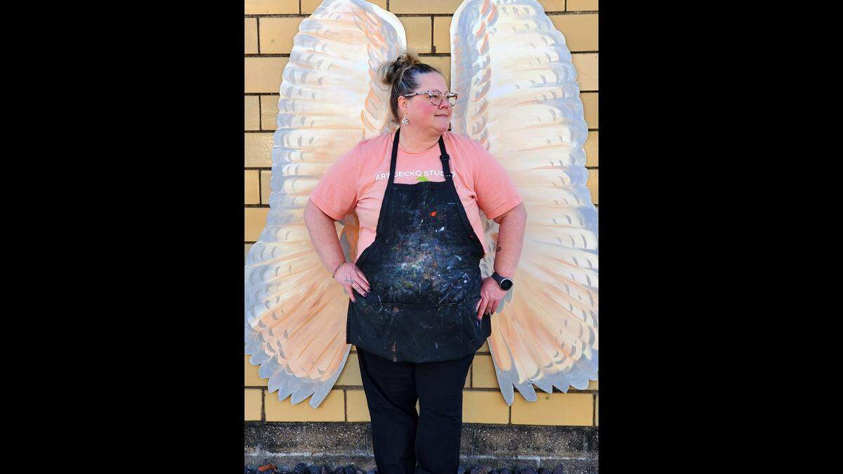 Cory Hallerbach stands before the owl wings at Art Gecko Creative Studio that were made by art teacher Hana Behrs.