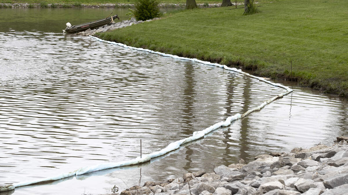 The lake at Marine Heritage Park in Marine was the site of an oil spill. Absorbent booms have been placed along several areas of the lake. A sheen of oil can be seen on the lake and oil coats grass and rocks along the shore.