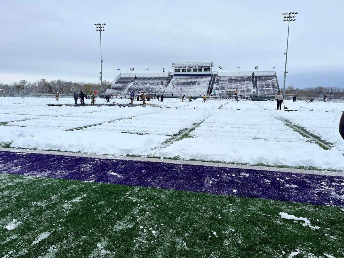 Members of Mascoutah High School clear the field of snow prior to Saturday’s IHSA Class 5A quarterfinal game against Peoria High School. The Indians led 21-14 at halftime but ultimately fell to the Lions 36-21.