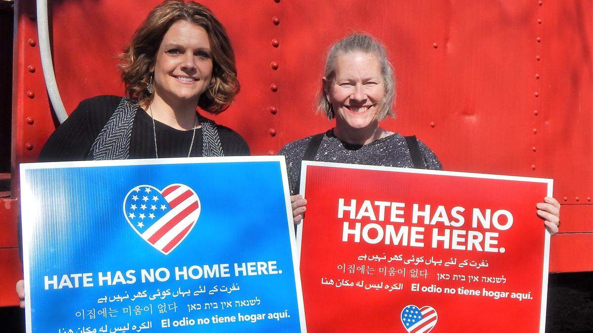 Jessica Gunther and Leslie Wolter hold yard signs for the "Hate Has No Home Here" campaign.