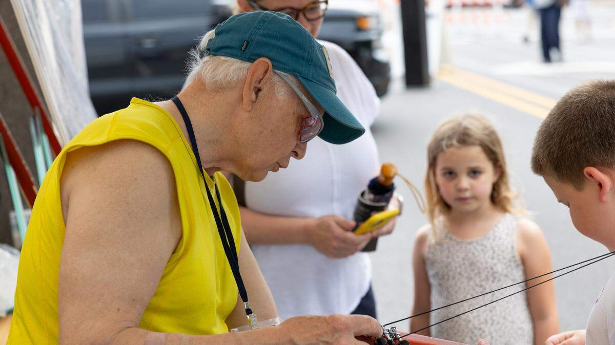 New Jersey-based instrument maker Bob McNally helps Connor Nester of Ohio using a ‘strum stick,’ an instrument that is part banjo and a dulcimer, during the first day of Belleville’s famous Art on the Square on May 17, 2024.