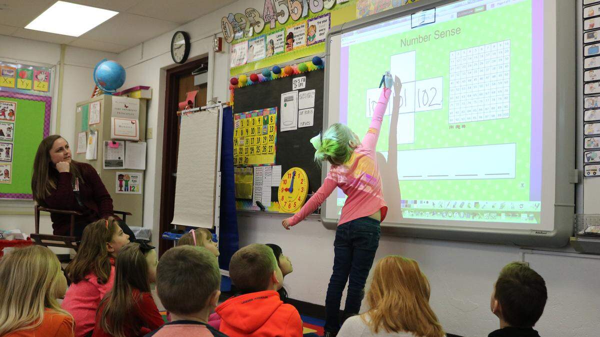 A student at Highland Primary School stretches to write on a Promethean board during a math lesson.