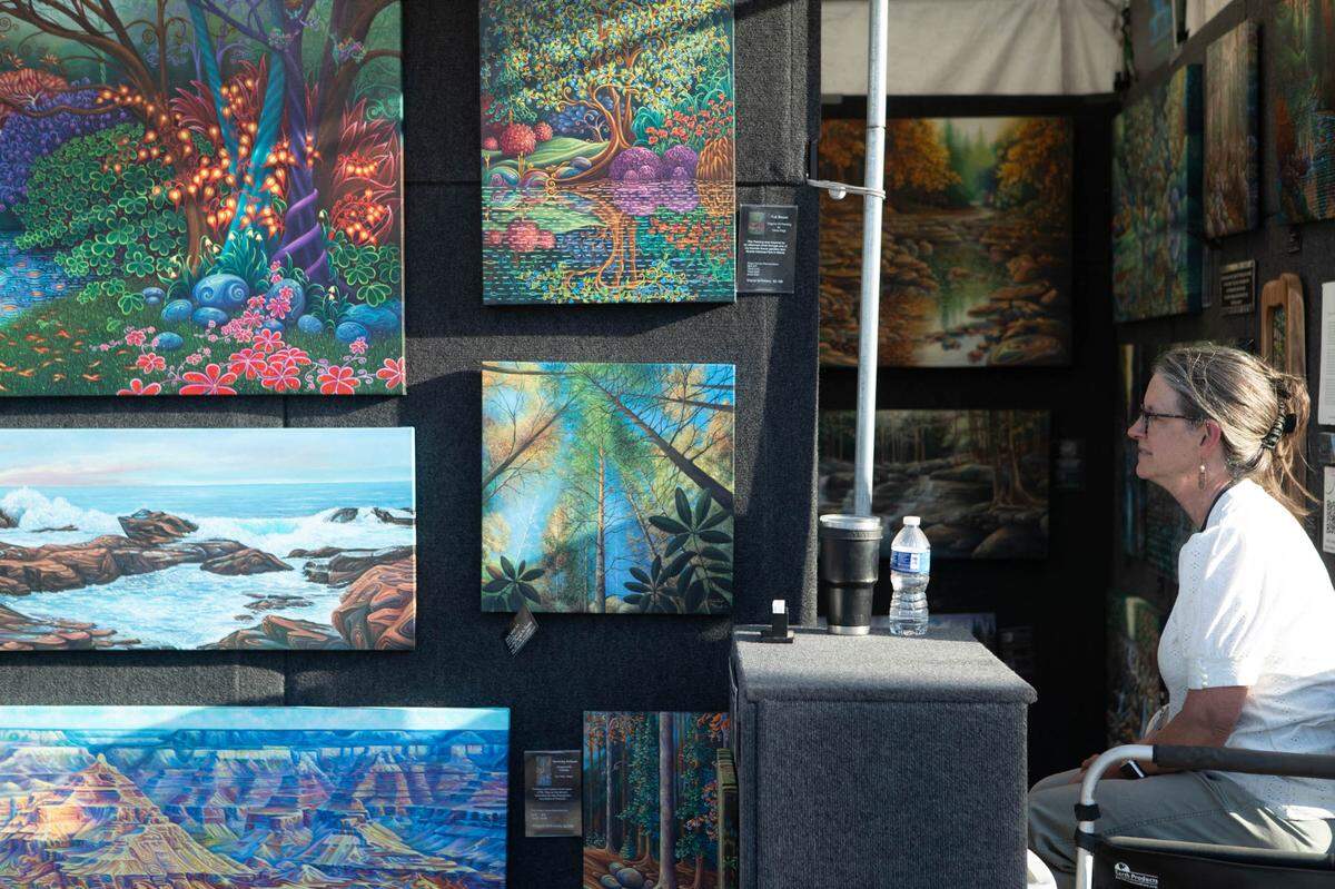 Artist Chris Abbot sits next to her paintings on Friday’s Art on the Square.