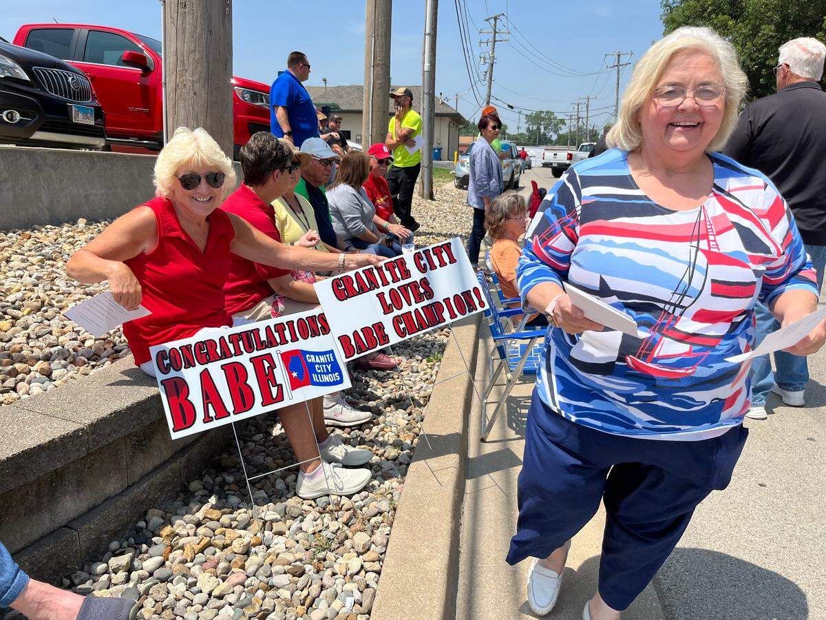 Paula Hubbard, right, hands out programs for the Babe Champion Parkway dedication ceremony on Friday in Granite City. Theresa Werner, left, made signs for the occasion.