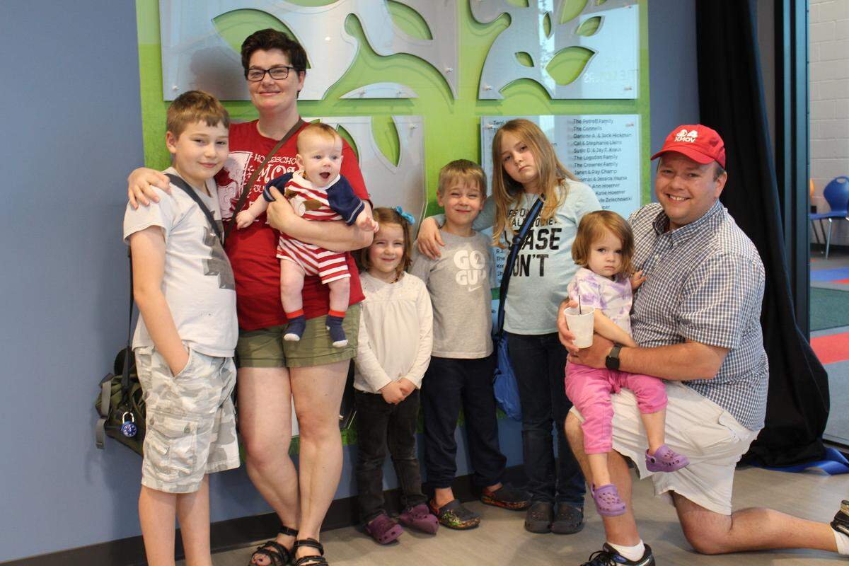 KMOV-TV personality Matt Chambers, kneeling right, poses in front of a wall honoring charter members of The Rec with his wife, Stephanie, and their six children.
