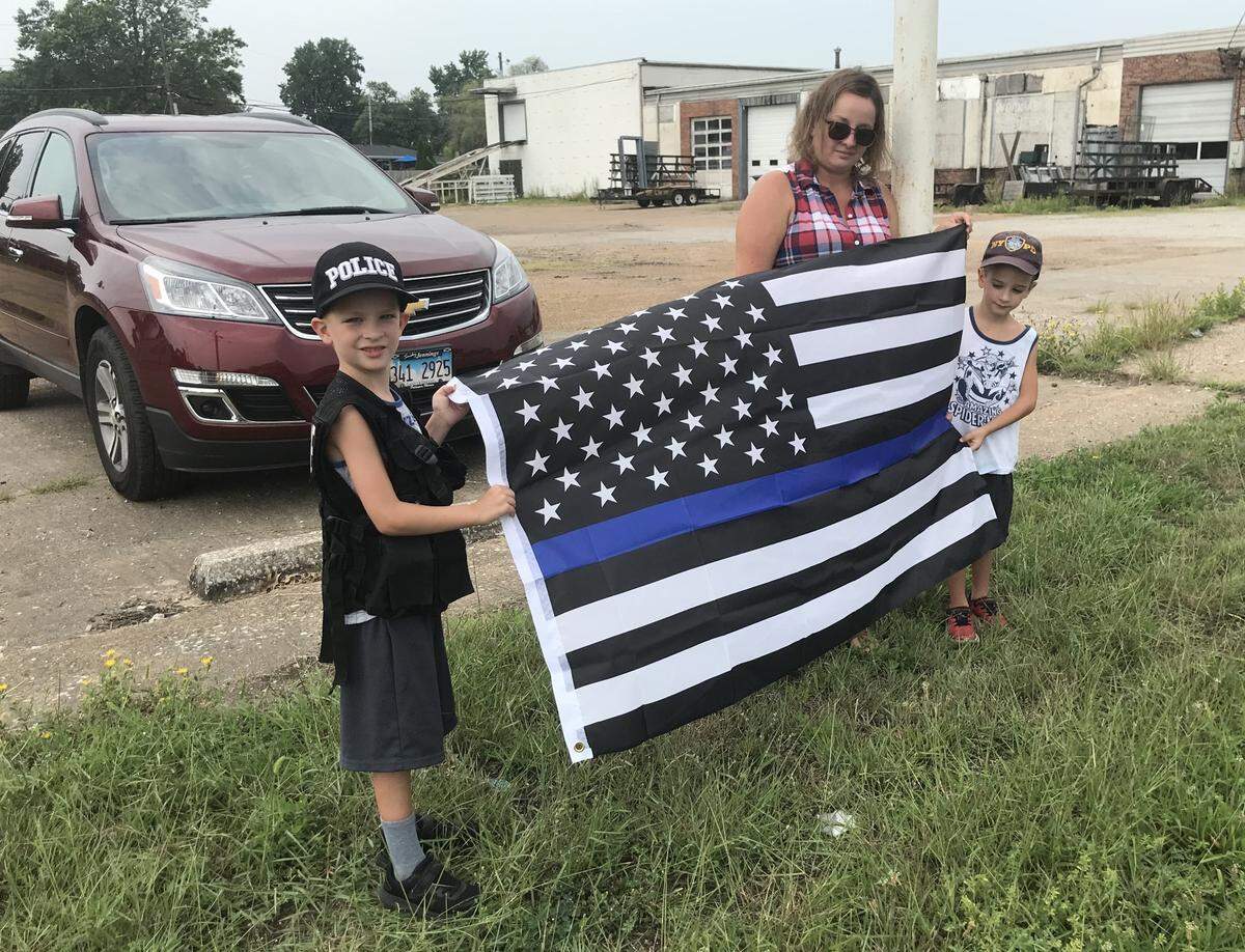 Julia Campbell and her 6-year-old twin sons, Colton, left, and Cooper, hold a “thin blue line” American flag along the route of a procession honoring fallen Brooklyn police officer Brian Pierce in Wood River on Friday.