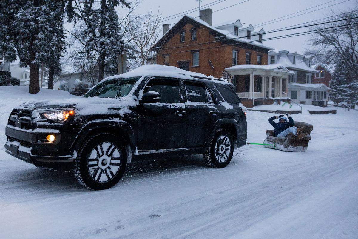 An SUV tows a passenger sitting on a couch down West College Avenue during a snowstorm on Sunday.