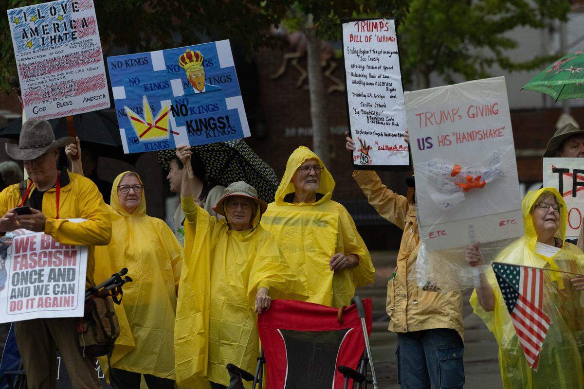 Protesters hold up signs as rain starts to pour along Belleville’s Public Square during the No Kings protest on Saturday.
