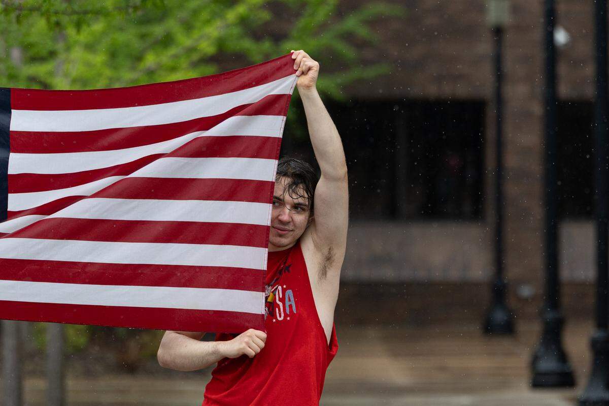 Sam Brosh of Swansea holds up an American flag as rain pours on a protest at Belleville’s Public Square. “Just seemed like the right thing to do,” Brosh said.