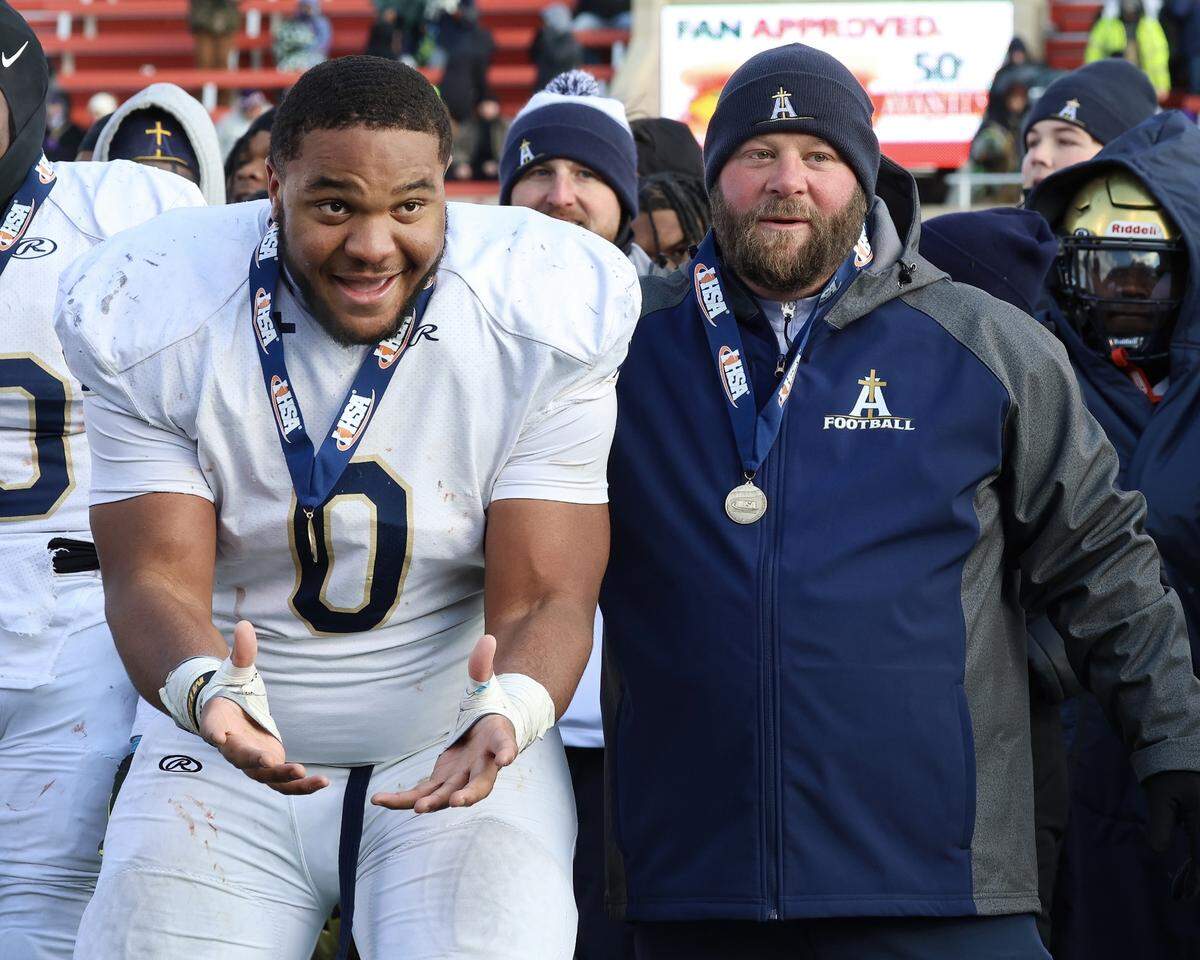 Althoff’s Jason Dowell and head coach Austin Frazier anxiously await the championship trophy after the Crusaders’ 57-14 win over Lena-Winslow for the IHSA Class 1A title at Hancock Stadium on the campus of the Illinois State University.