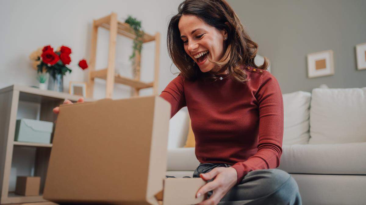 Excited woman opening a cardboard box in her living room, discovering a pleasant surprise