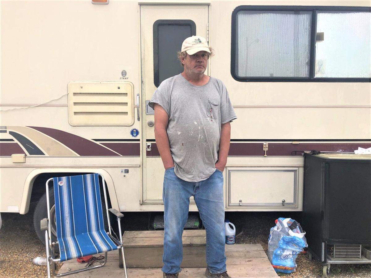 Gregory Gabelman stands in front of the camper he and his son are staying in parked in a gravel lot near Babe’s Fish Wagon. They were displaced from their trailers in the summer. The village has since condemned the trailer park where they lived.