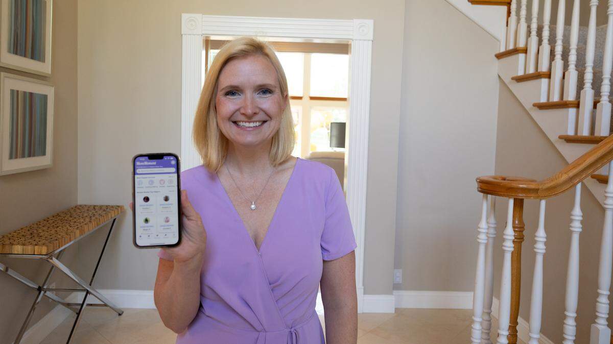 Amanda Hausmann holds up her phone to display MomMoment, a new app that helps crowdsource help from other mothers looking to lend a hand.