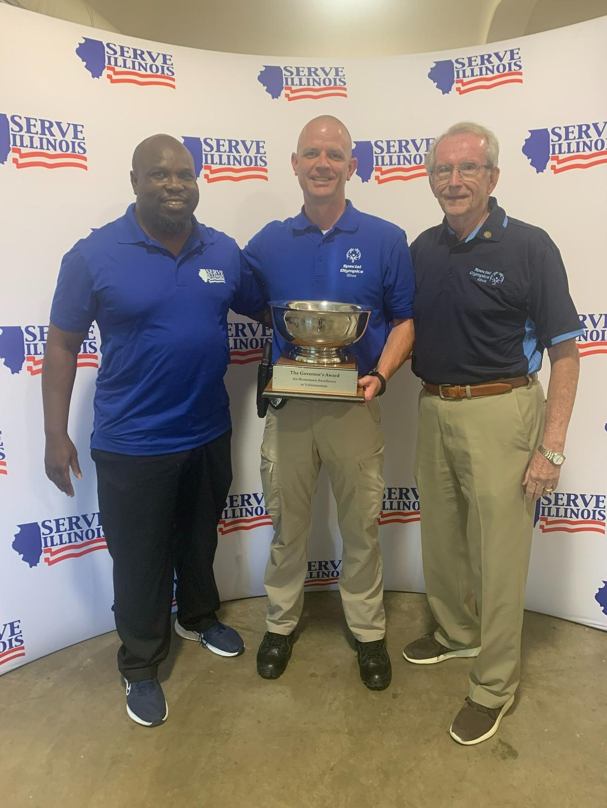 A representative of Serve Illinois presents the Governor’s Cup to O’Fallon Police Detective Nick Schmidt, the Special Olympics coordinator, and O’Fallon Mayor Herb Roach. For the city-wide efforts supporting the Special Olympics, O’Fallon was among four Governor’s Hometown Awards finalists. O’Fallon ultimately brought home the Governor’s Cup after winning over the Governor’s Hometown Awards judges with their presentation. The traveling trophy was awarded at the Illinois State Fair in Springfield on Thursday, Aug. 18.