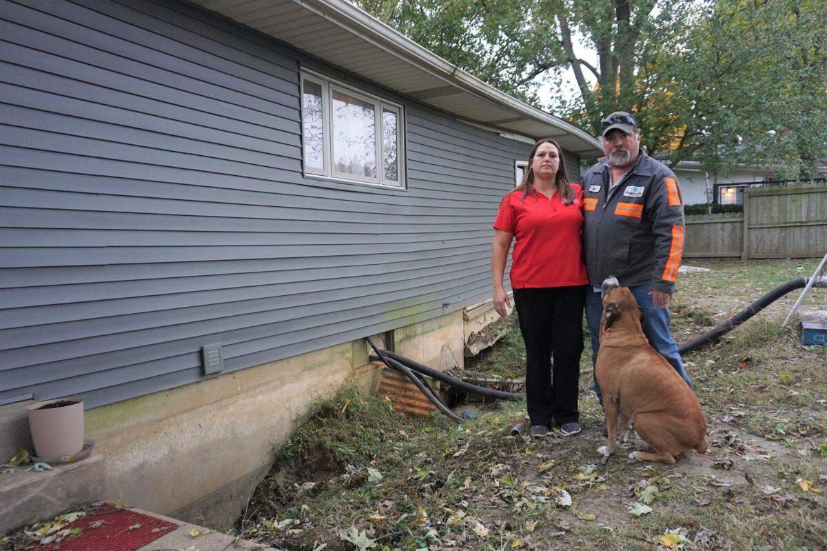 Robert and Tina Rhymer pose for a picture in the back of their home in East Cape Girardeau, Illinois, with their dog, Harley. A sink hole formed in June during flooding and has ruined their home.