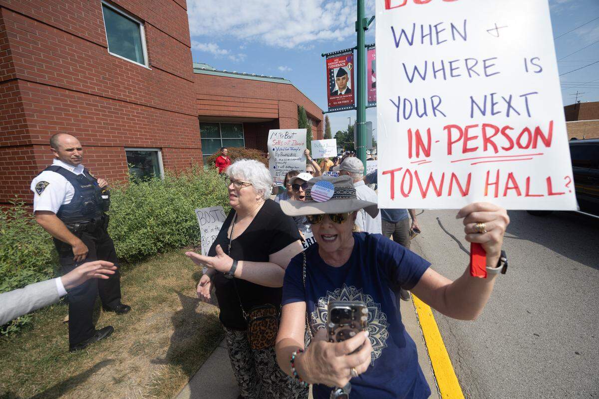 Protestors outside of the O’Fallon police dept. chase U.S. Mike Bost to a waiting police car, demanding to know when his next public town hall would be.