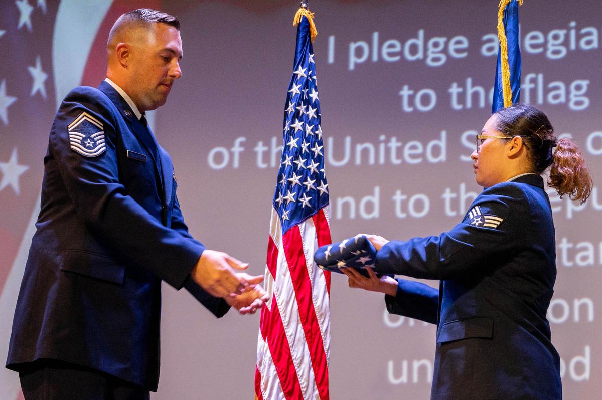 U.S. Air Force Senior Master Sgt. Austin Winegardner, 375th Civil Engineer Squadron heavy repair superintendent, hands an American Flag to Senior Airman Harlyn Truong, 375th Logistics Readiness Squadron traffic management, during a U.S. Naturalization and Oath of Allegiance Ceremony on Scott Air Force Base. Lt. Col. Ryan Leblanc, 375th CES commander, held a naturalization ceremony in honor of the eight Airmen in completing the process to obtain their U.S. citizenship with the help of the military.