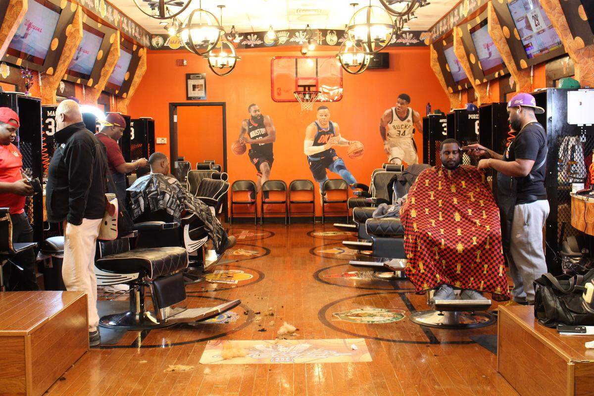 Kenneth Moran, right, trims Curtis Hill’s hair and Juan Garth, second from left, trims Terrance Jones’s hair at All Star Kutz, a new basketball-themed barbershop at St. Clair Square.
