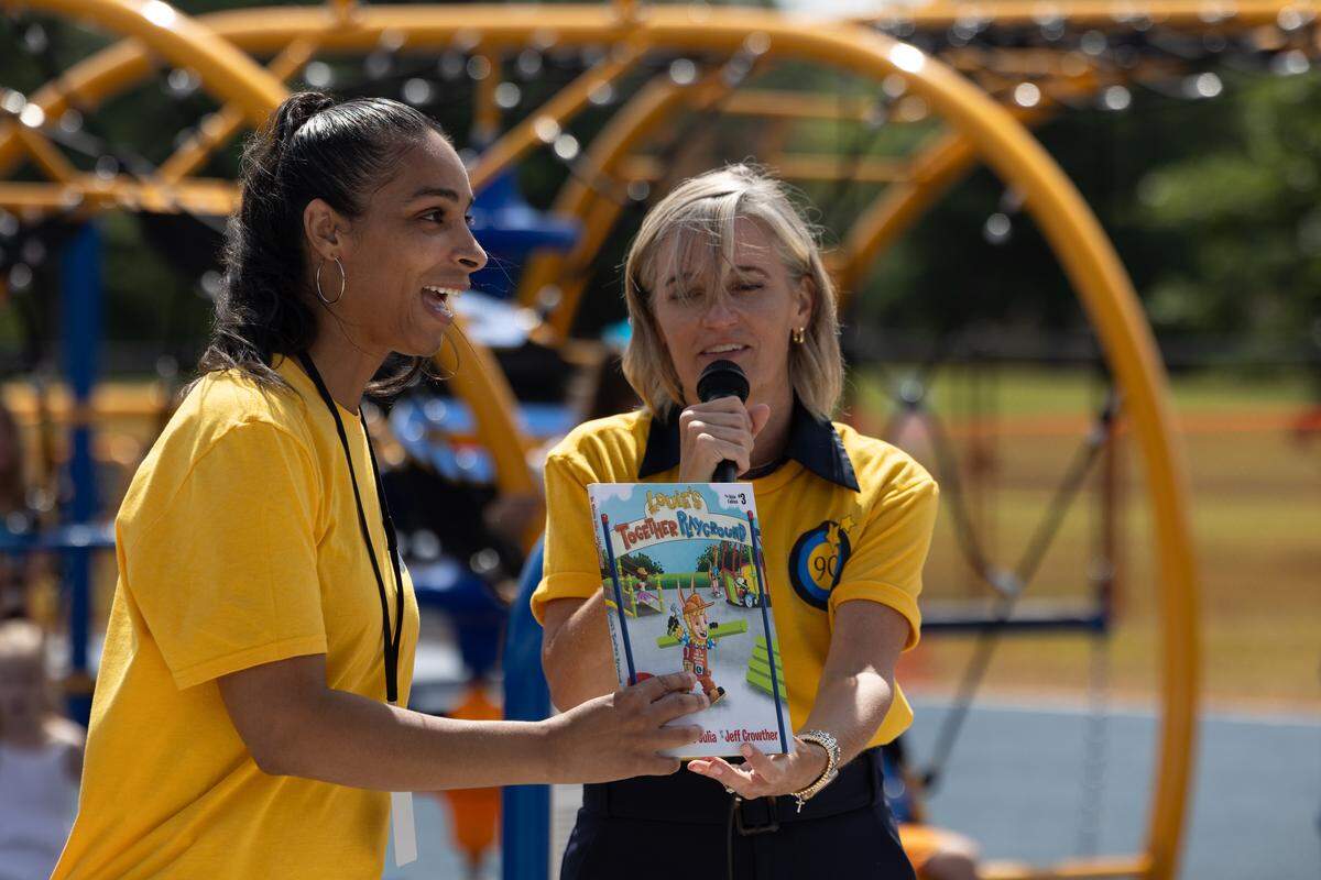 Carrie Hruby (right) hands a book about inclusive playgrounds to Mara Hamilton, principal of Hinchcliffe Elementary, during a ribbon cutting ceremony for the school’s new inclusive playground.