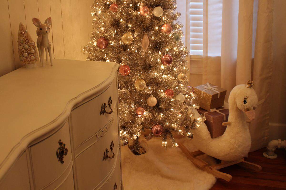 The nursery of the Hettenhausen home in Belleville features a child’s swan-shaped rocking chair filled with glittery gold gifts under a silver tinsel Christmas tree.