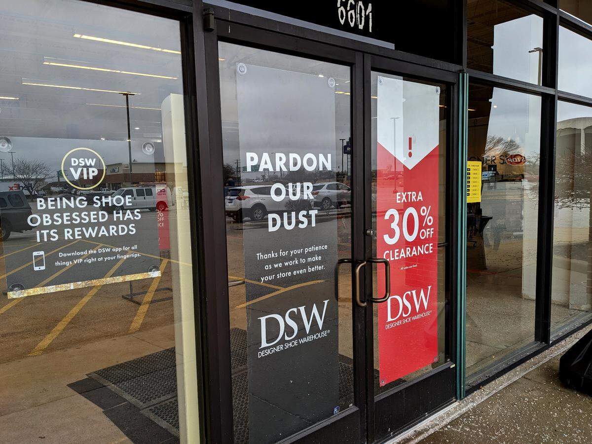 Door signage at DSW lets customers know about the current construction work inside. The store is downsizing to accommodate two new stores next door.