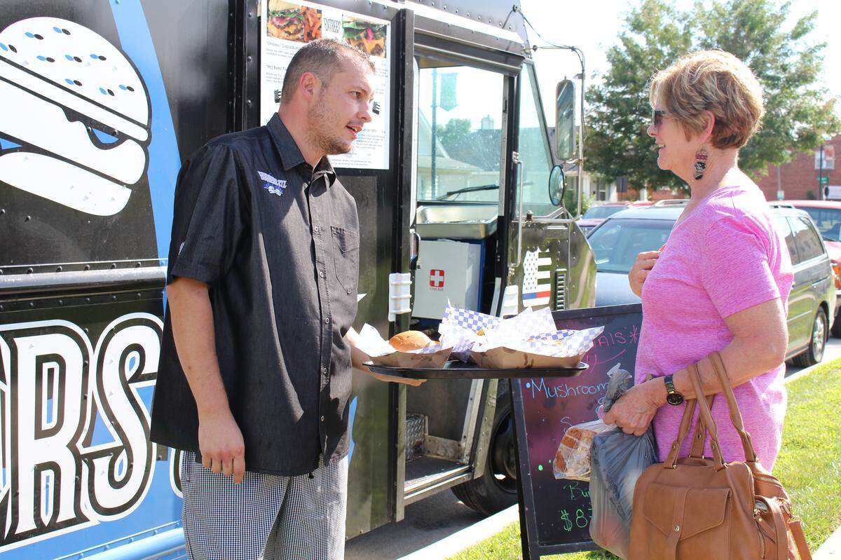 Matt Foley, left, owner of the Burgers STL food truck, shows some of his menu items to a shopper at Maryville Farmers Market, which operates one day a month in Collinsville.