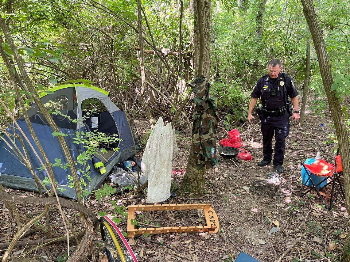 Swansea Police Chief Matt Blomberg surveys a squatters camp with a tent, chair, plastic tubs of clothing and a barbecue grill in woods along the MetroBikeLink Trail last year.