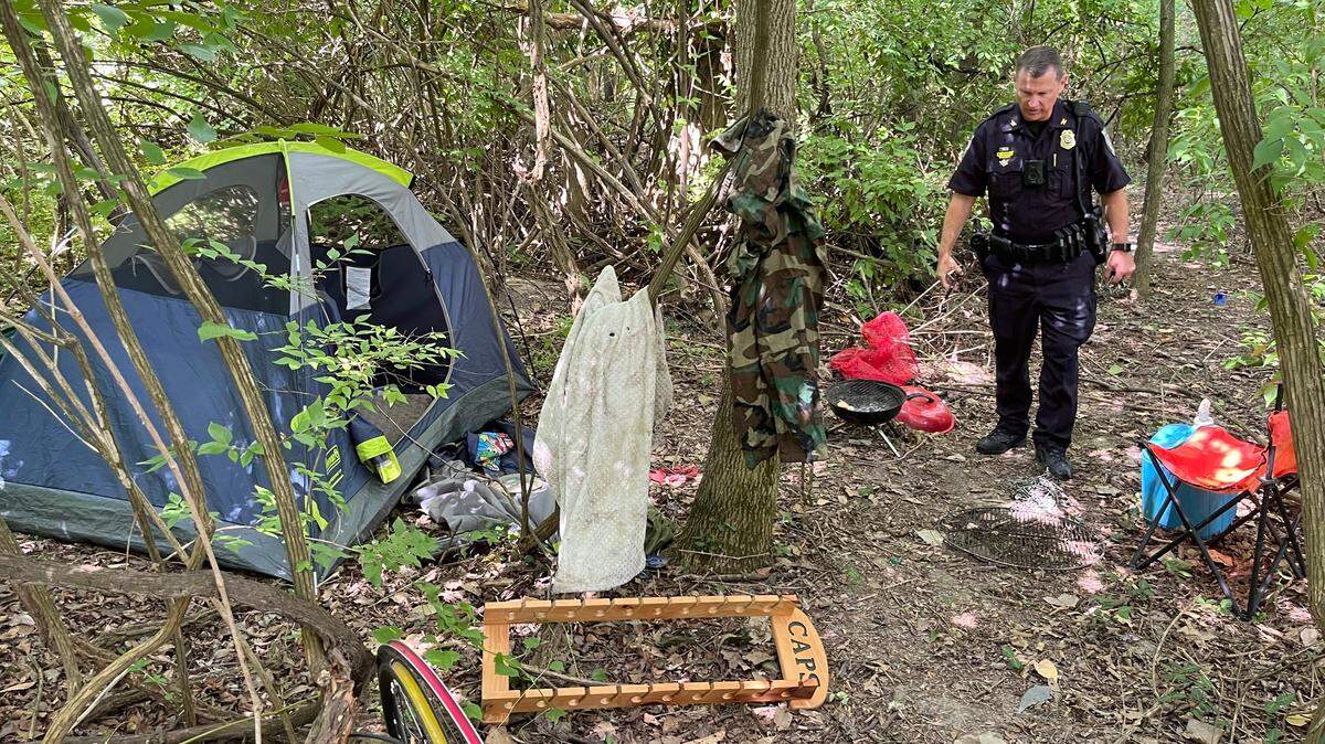 Swansea Police Chief Matt Blomberg surveys a squatters camp with a tent, chair, plastic tubs of clothing and a barbecue grill in woods along the MetroBikeLink Trail last week.