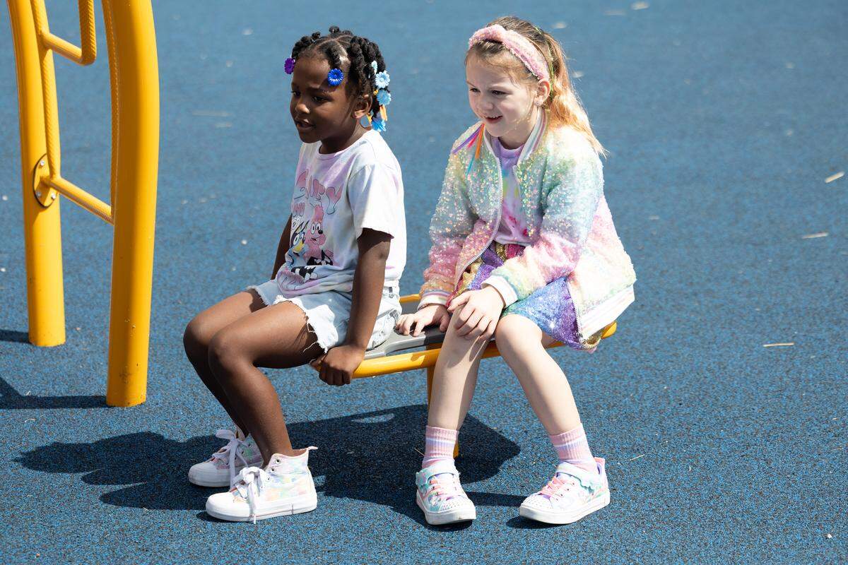 Children sit on a low stool big enough for two people during recess. The stool is part of a newly opened accessible playground meant to be inclusive to children of all capabilities. 