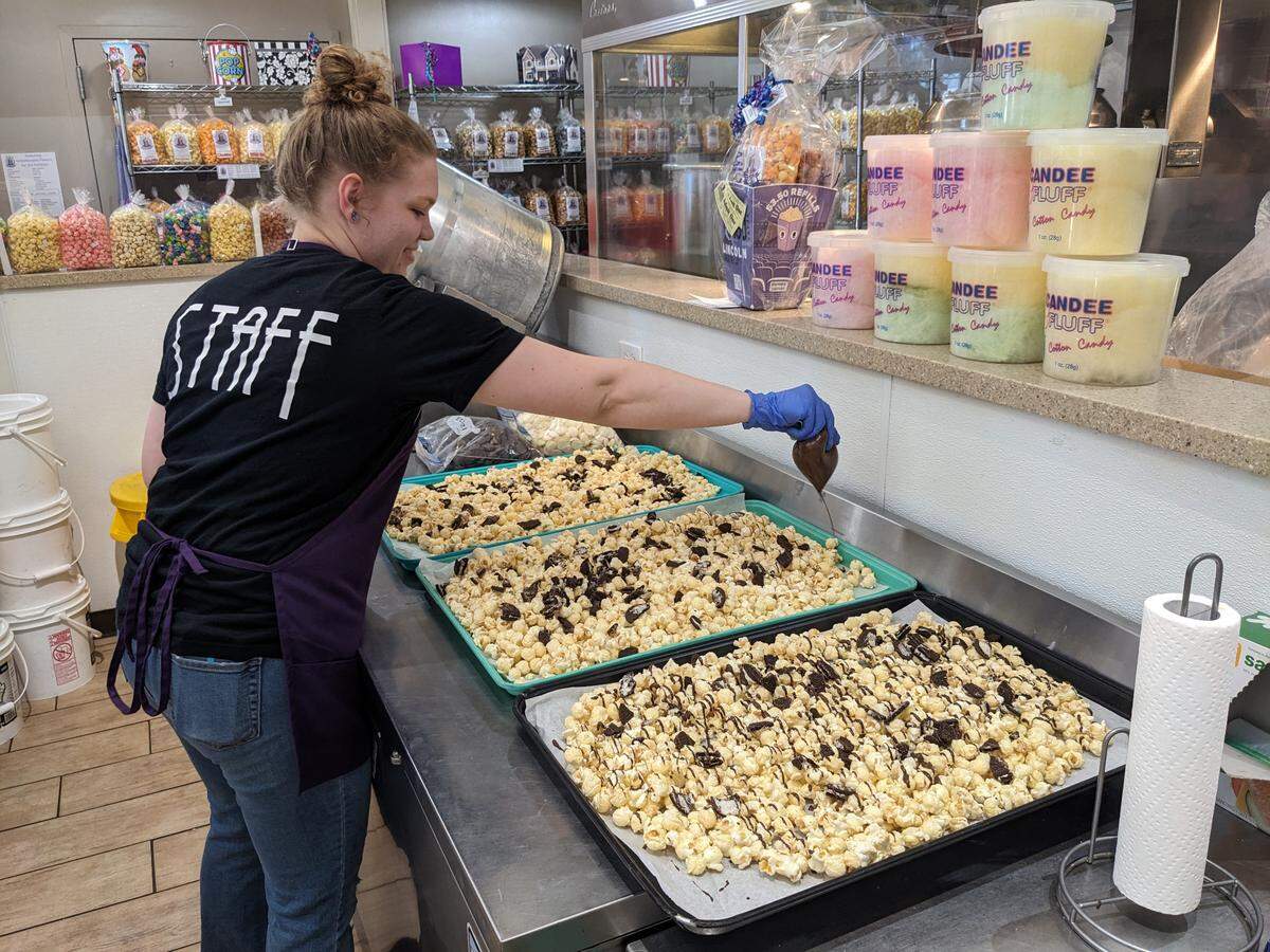 August Logan drizzles chocolate over Oreo-covered vanilla popcorn to finish off the cookies ‘n cream flavor at Abe’s Gourmet Popcorn in downtown Belleville.