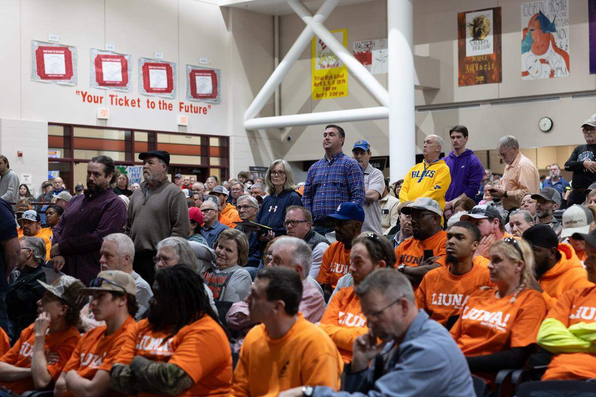 A queue of people wait to ask questions during a meeting about a possible data center development in Troy. Some opponents wore anti-data center shirts or held signs. Supporters from local unions wore matching orange shirts.