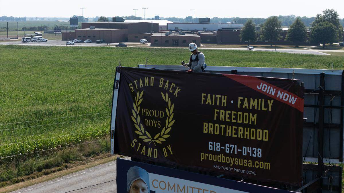 A worker adjusts the position of a Proud Boys billboard on old U.S. 50, just outside Breese, that has caused controversy. Central Community High School can be seen in the background.