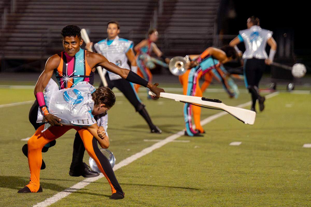 A Boston Crusaders color guard member spins a rifle while a horn line member holds on during their show “BOOM” at Belleville West High School on Tuesday, July 22, 2025, in Belleville.