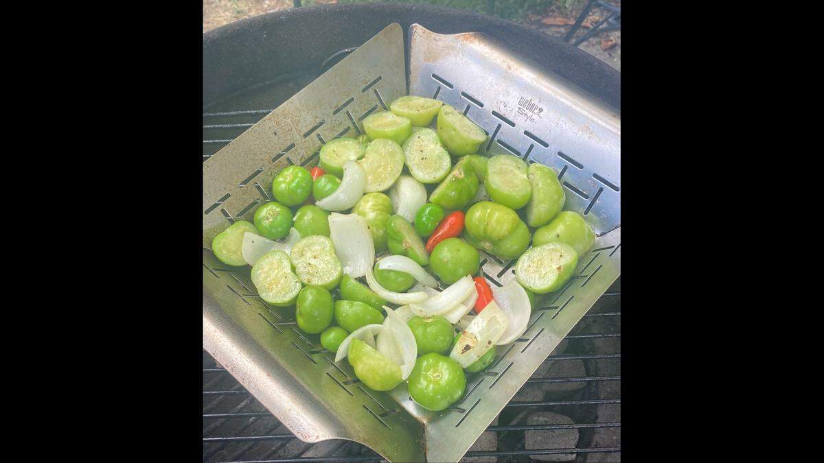 Grill pan filled with tomatillos, serrano peppers and onions. These serranos peppers are red but you can use green ones as well for grilled tomatillo salsa.