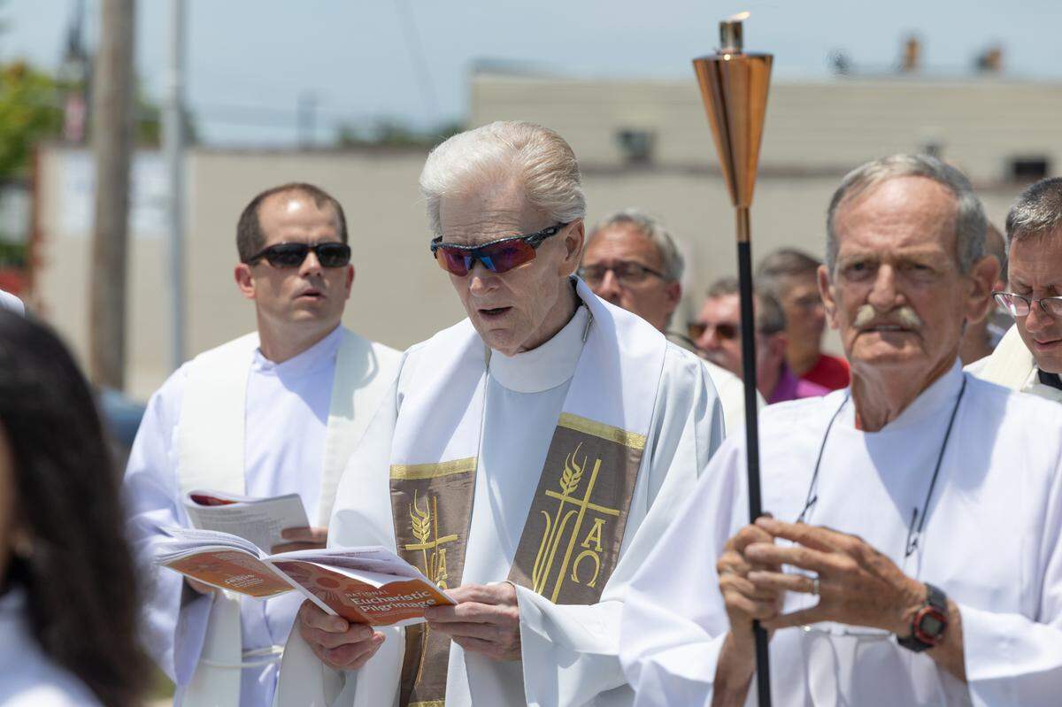 Rev. John Beveridge sings hymns during a procession from St. Peter’s and Paul’s Catholic Church to a nearby cemetery of the same name in Collinsville, Ill. on July 8, 2024. The procession is part of a nationwide eucharist pilgrimage, with Catholics traveling from San Francisco to the endpoint of the pilgrimage, Indianapolis, picking up fellow pilgrims along the way.