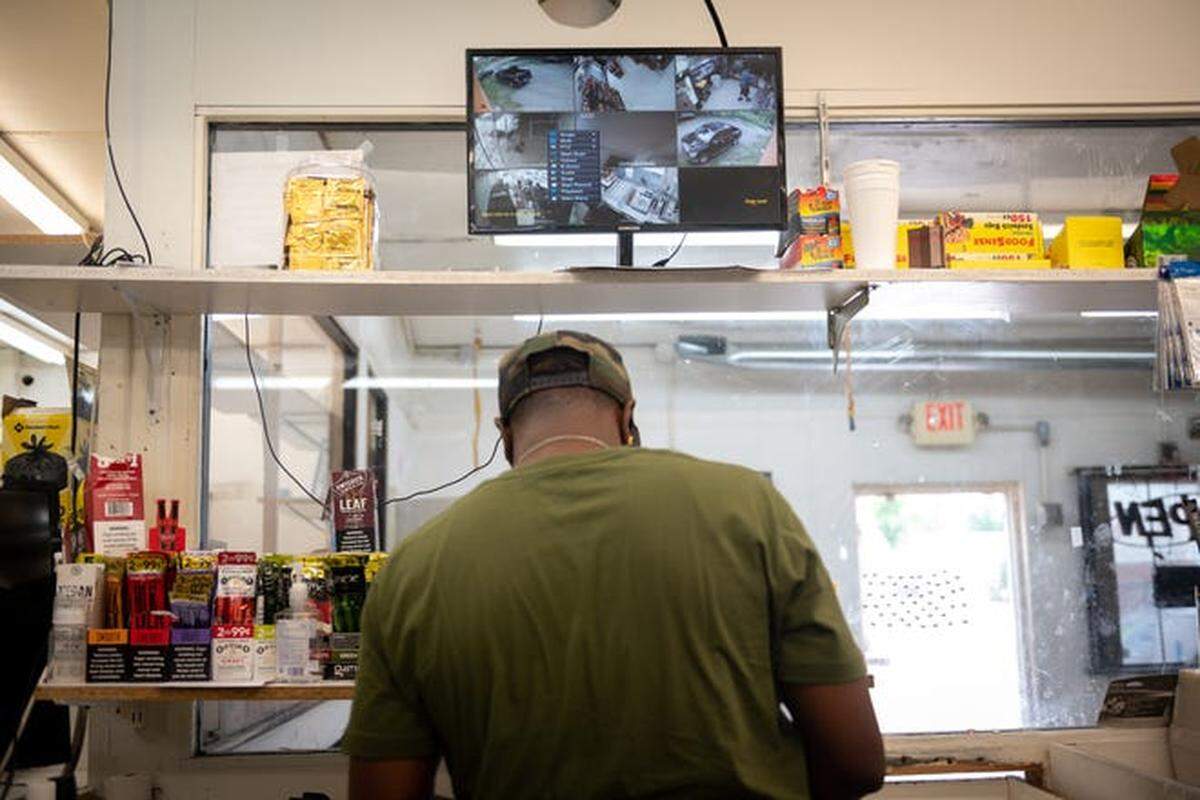 Shantz Rias stands beneath a surveillance camera display.