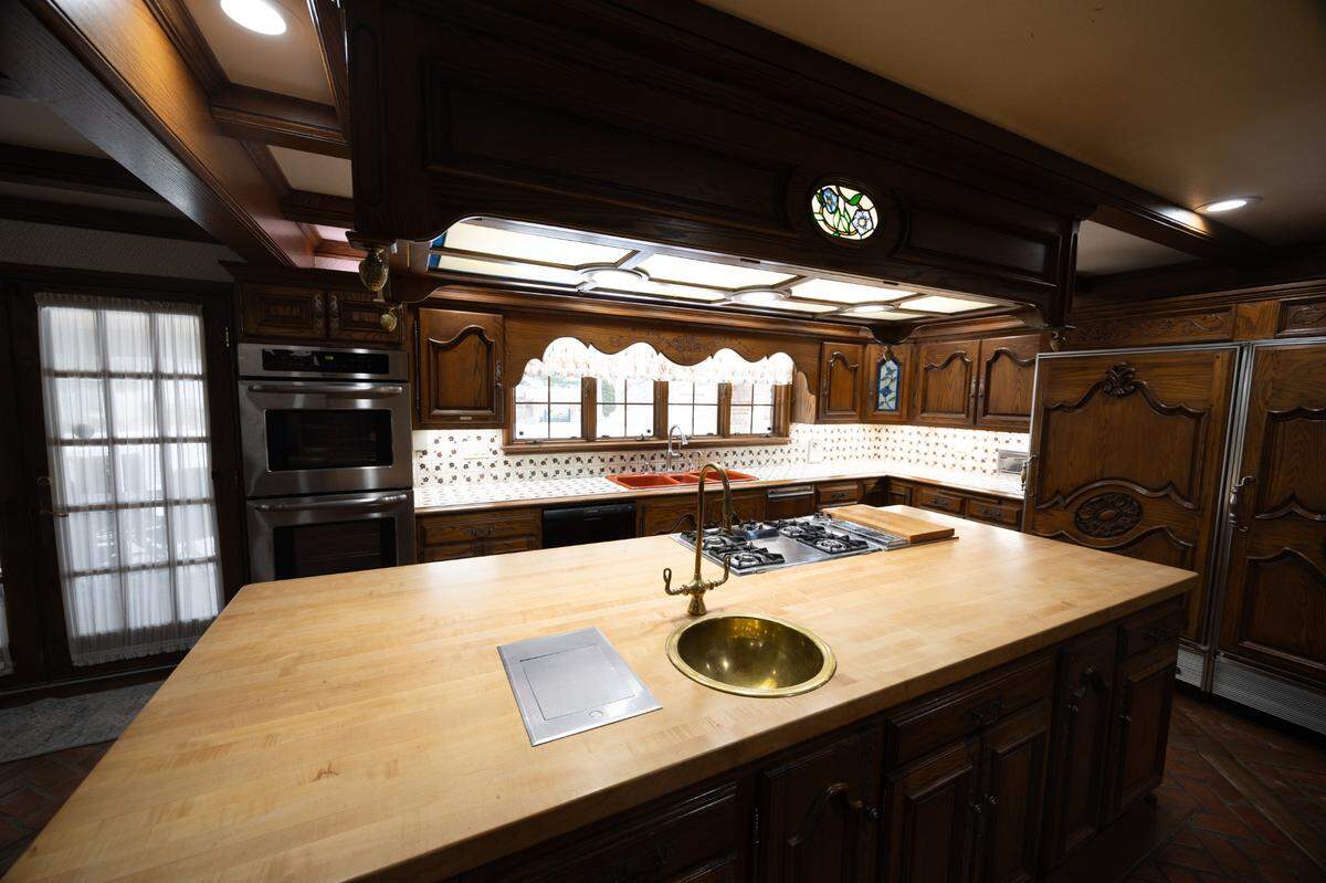 The kitchen features an island, a double oven, an custom-made cabinetry.