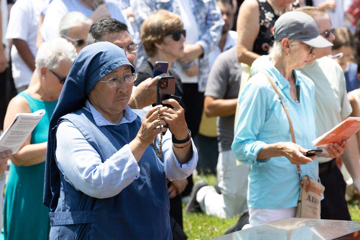 A nun takes photos on her phone while holding a rosary at Ss. Peter and Paul Cemetery in Collinsville, Ill. on July 8, 2024. The procession is part of a nationwide eucharist pilgrimage, with Catholics traveling from San Francisco to the endpoint of the pilgrimage, Indianapolis, picking up fellow pilgrims along the way.