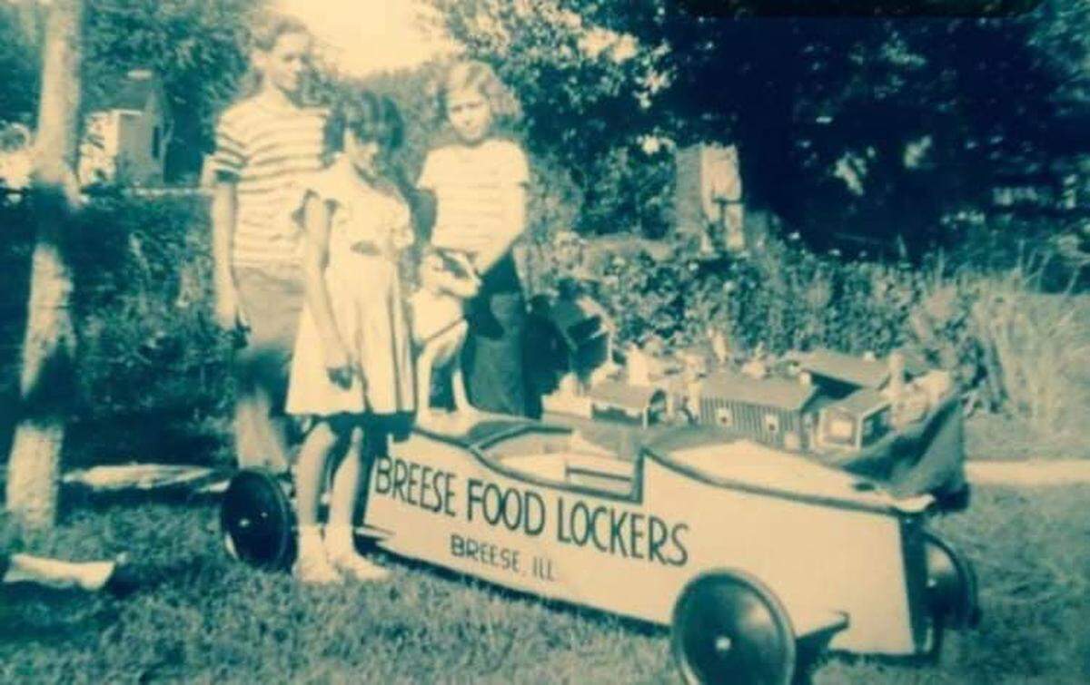Barbara Koch, center, poses with Rich Hellige and his sister, Mary, next to a soapbox derby car advertising Hellige’s in the 1940s.