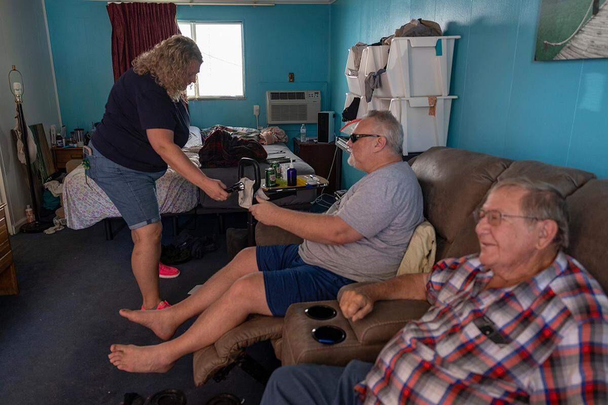 Stephen Casner, center, was diagnosed with early onset Parkinson’s disease, and Heather is his primary caregiver. The couple and Stephen’s father, Fred Casner, spend time in a motel room they converted into a break room where Stephen can be near Heather during the day.