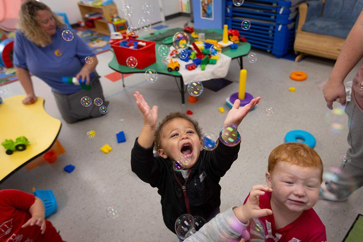 Bryce Clemons and Harper Watkins play with bubbles as Heather cleans toys.