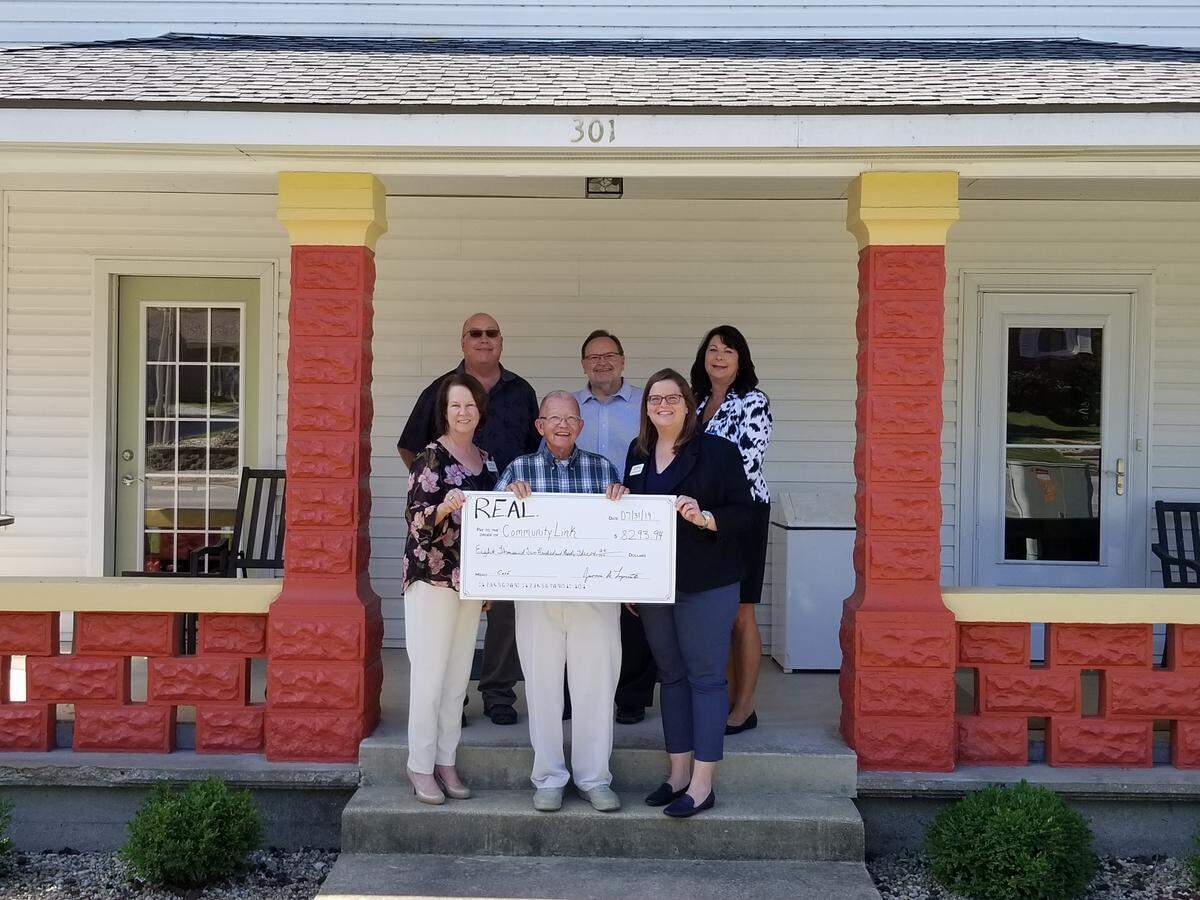 A ceremonial check-passing ceremony at The Red Porch includes, front row left to right, Barb Nelson, Community Link director of adult day programs; Eldon Ahner, REAL president; Lynn Huelsmann, Community Link executive director; and, back row, REAL group members Gordon Hoerchler, Jim Lopresto and Cheryl Smith.