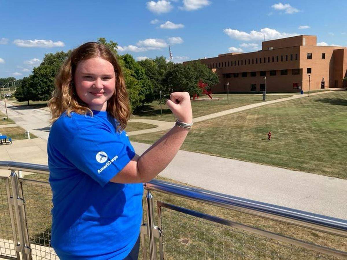 Morgan Gillham, a Belleville AmeriCorps service worker, strikes a pose made famous by the Rosie the Riveter character during World War II. Gillham attends Southwestern Illinois College, shown in the background.