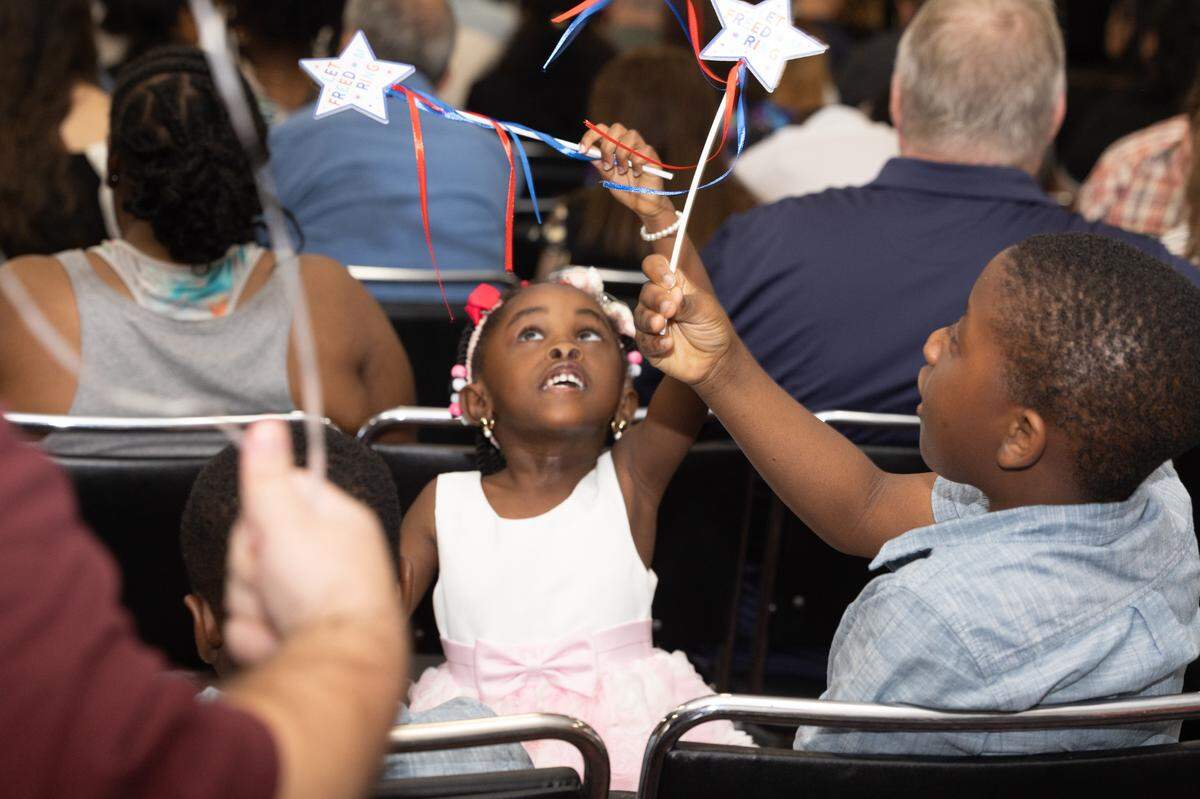Children play with wands that say “let freedom ring” on them at a naturalization ceremony in Collinsville.