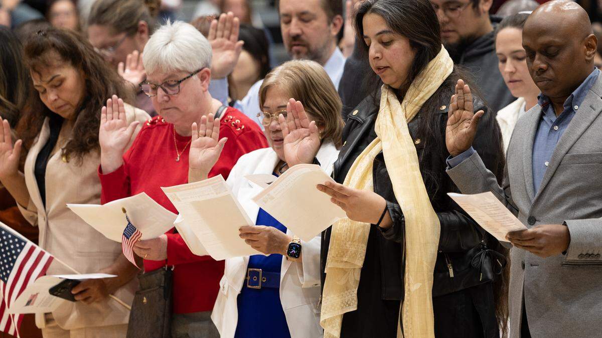 Soon-to-be Americans take an oath to uphold the constitution and disavow any foreign allegiances during a naturalization ceremony at Belleville West High School on Friday.