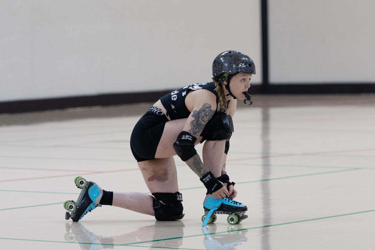Abigale Clare, who goes by the derby name “Abditude,” ties her skate while simultaneously coordinating drills during a Troy practice.